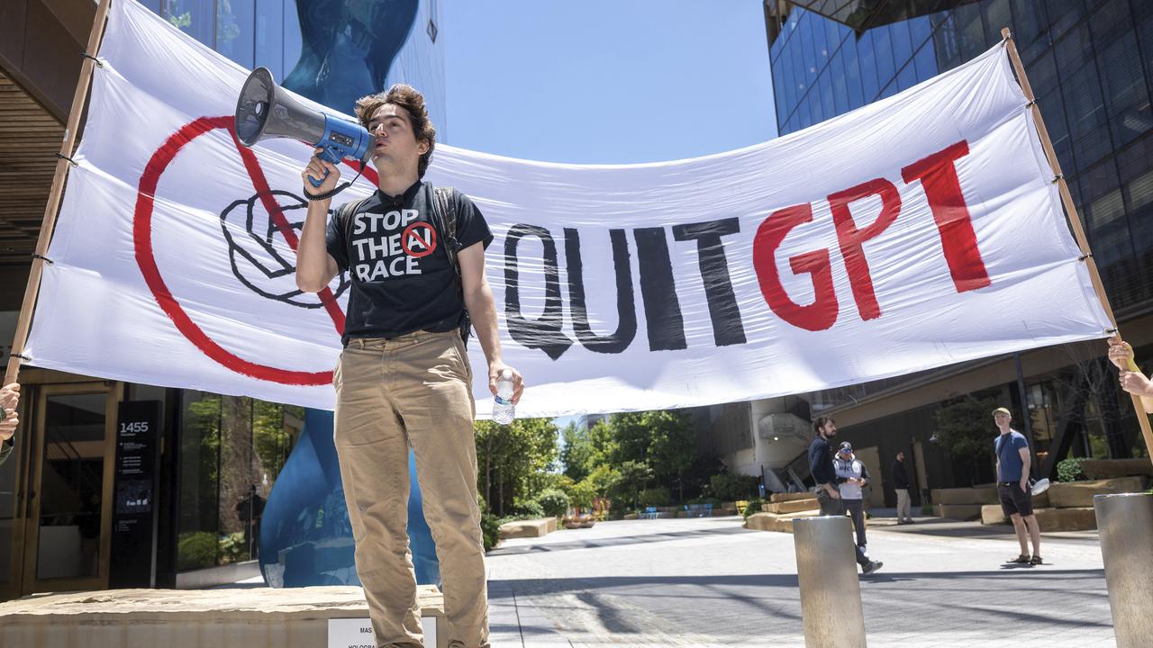 Protester speaking through a megaphone in front of a large Quit GPT banner